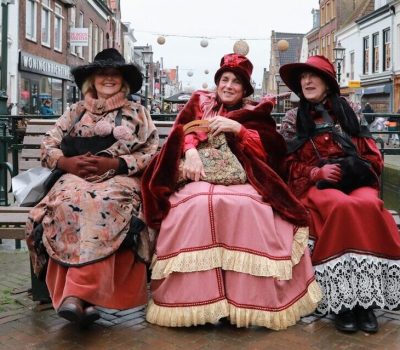 Drie damens zitten op een bankje verkleed in historische kledij